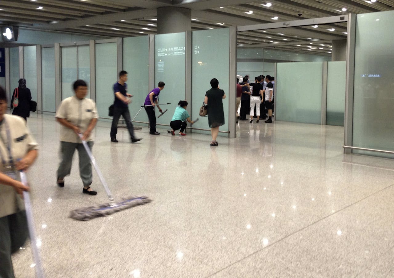 Schoonmakers vegen de vloer en de ramen schoon, na de ontploffing van een vuurwerkbom op het vliegveld van Peking.